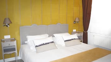A neatly made bed with white bedding and two pillows, a bedside table with a lamp, and a wall with a yellow panel.