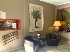 A hotel lobby with a framed cityscape, a tree mural, a small table with a vase of flowers, two leather chairs, and a lamp.
