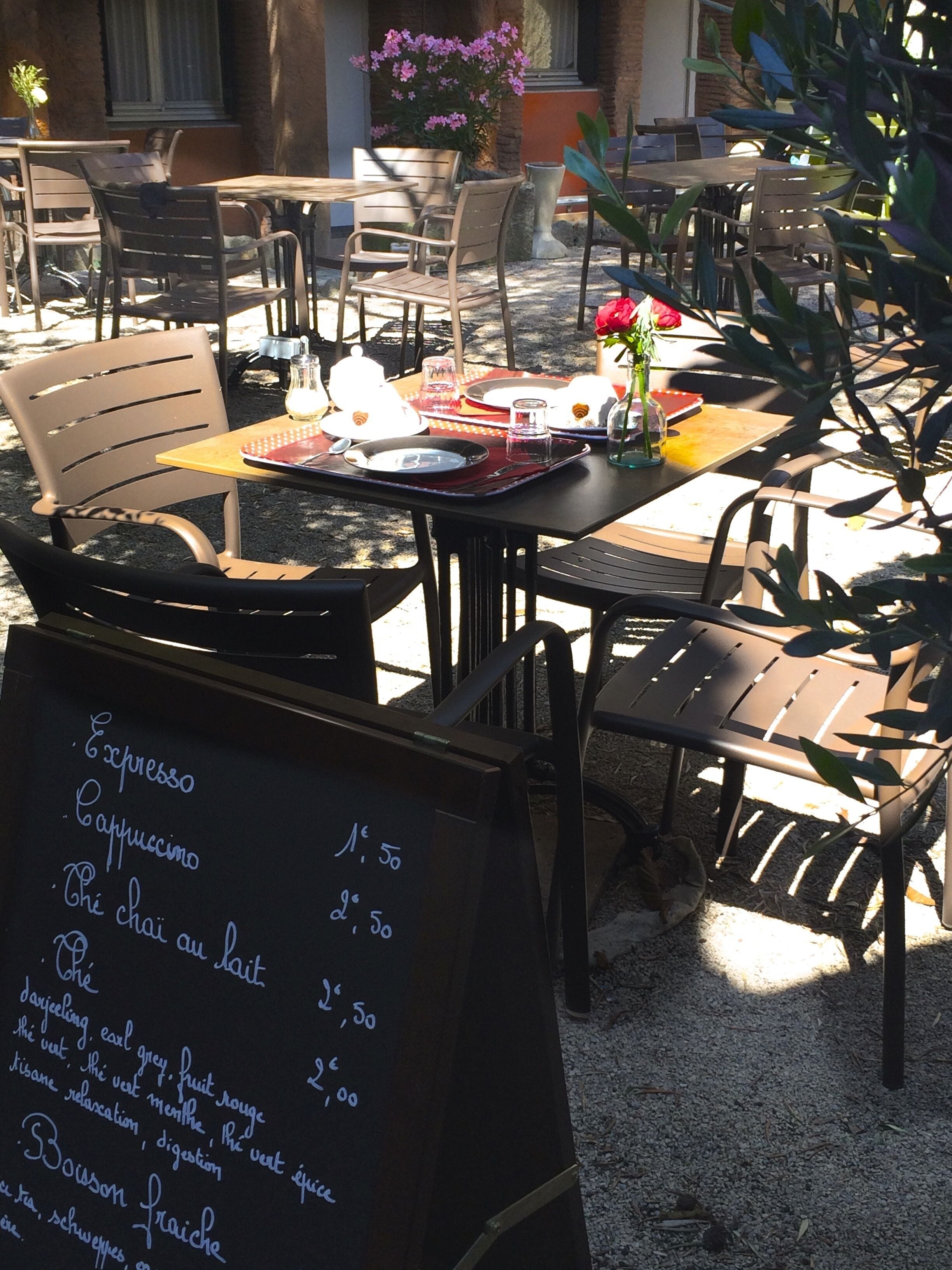 An outdoor café with tables and chairs, a menu board, and potted plants.