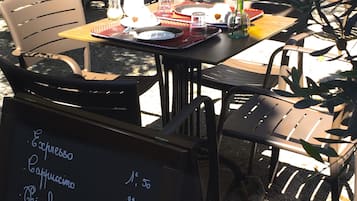 An outdoor café with tables and chairs, a menu board, and potted plants.