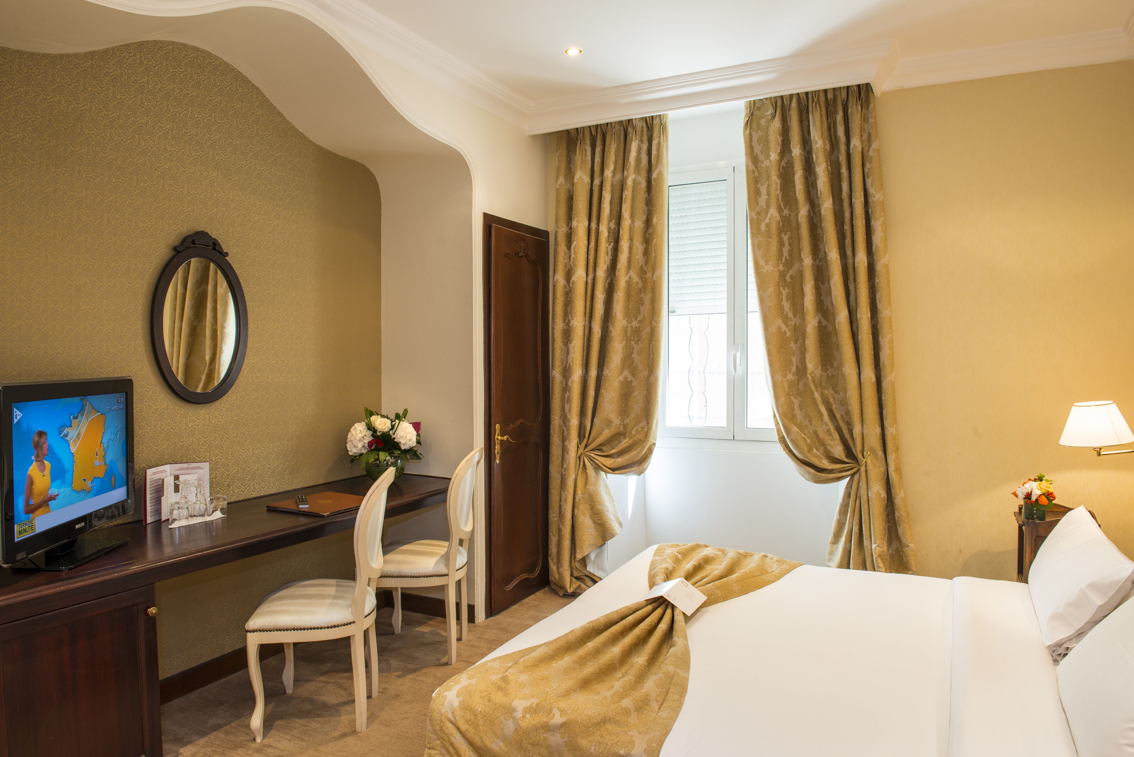 A hotel room with a bed, a desk with a chair, a television, and curtains.