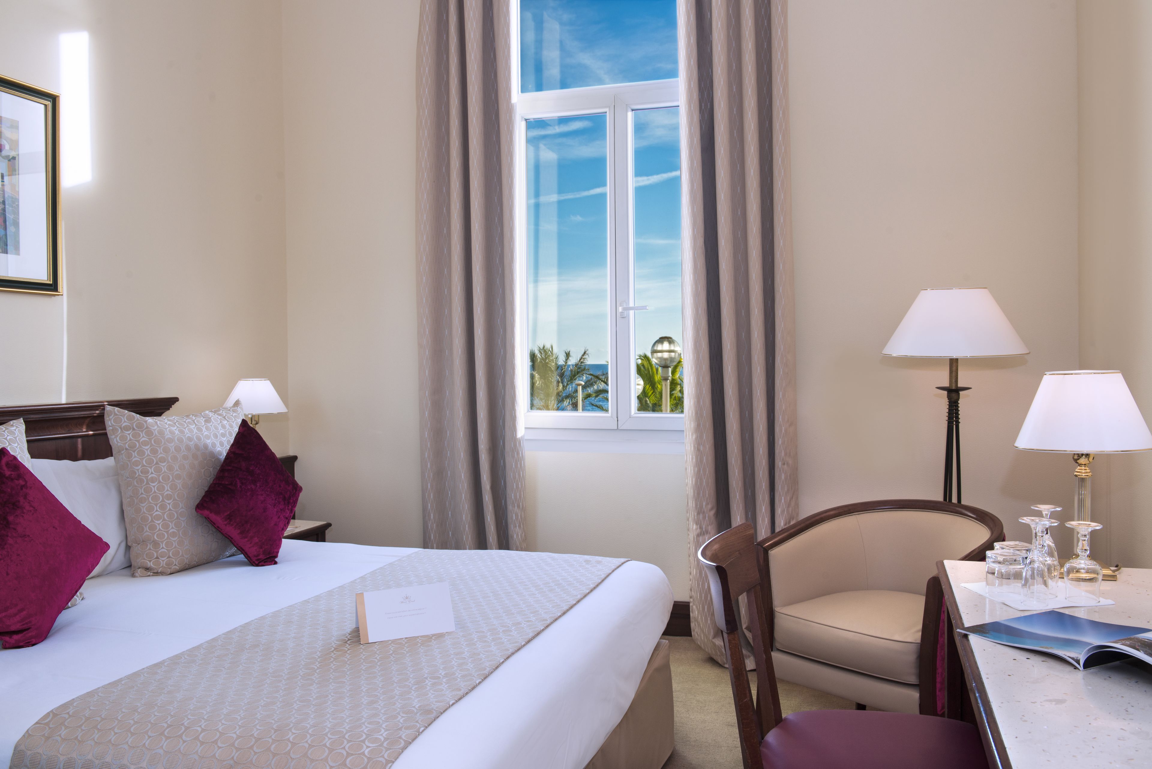 A hotel room with a bed, a chair, a table with a lamp, and a window with curtains.