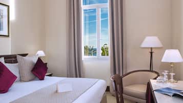 A hotel room with a bed, a chair, a table with a lamp, and a window with curtains.