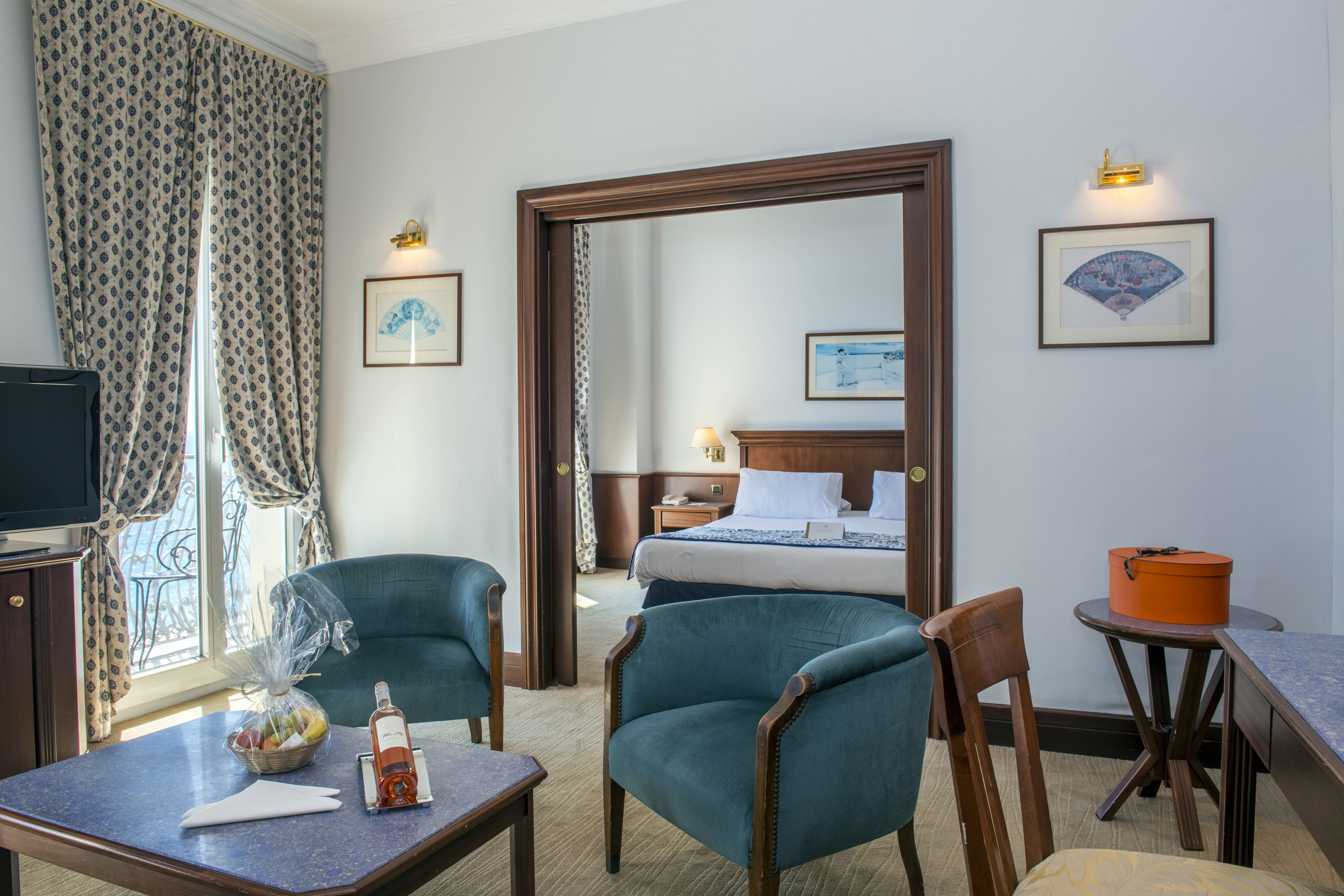 A hotel room with a bed, two chairs, a small table, a TV, and a window with curtains.