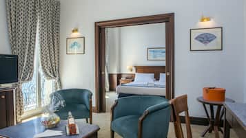 Habitación de hotel con cama, dos sillones, una mesita, televisor y ventana con cortinas.