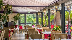 An indoor cafe with wicker furniture, red chairs, and potted plants.