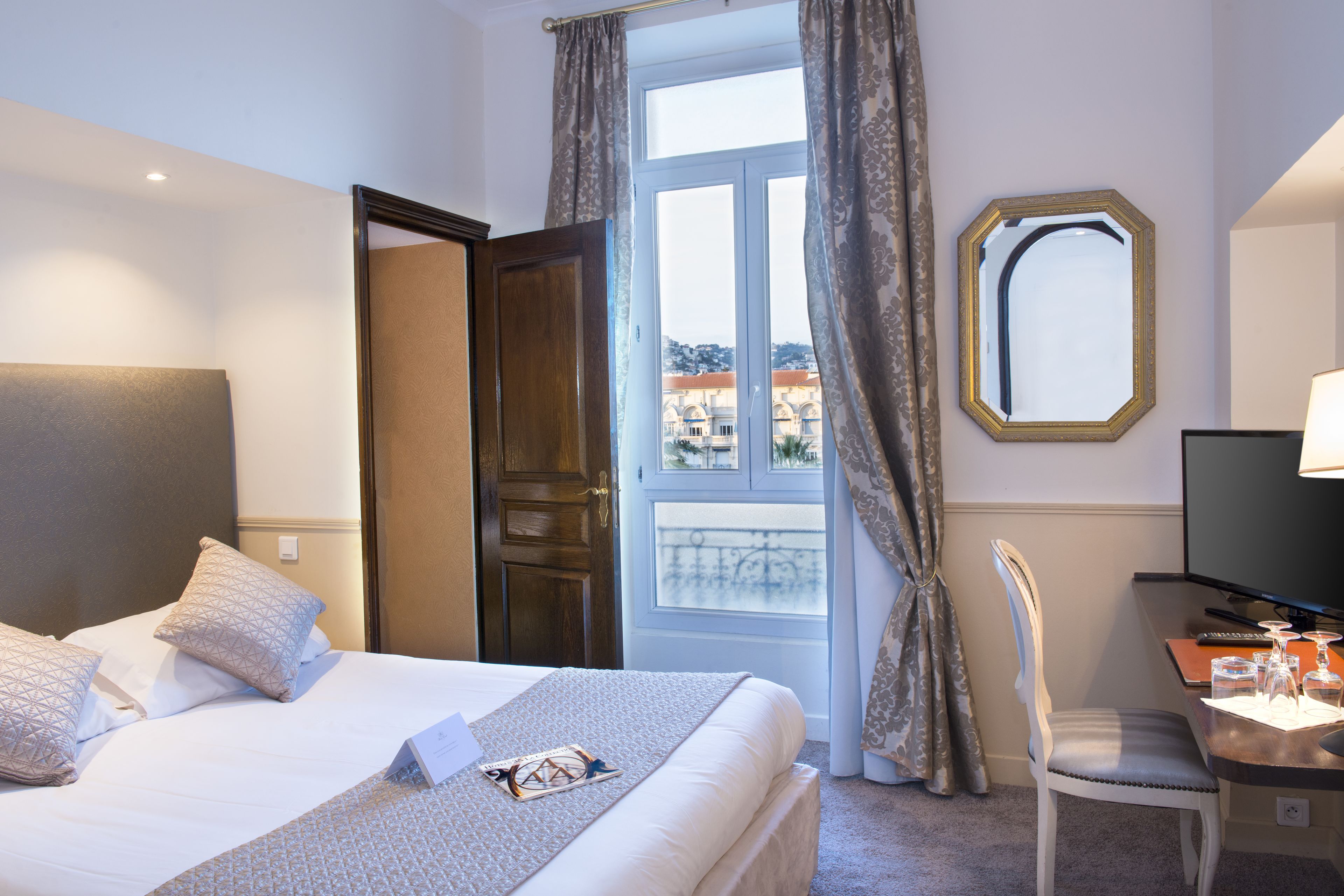 Una habitación de hotel con una cama, un escritorio con silla, televisión y ventana con cortinas.