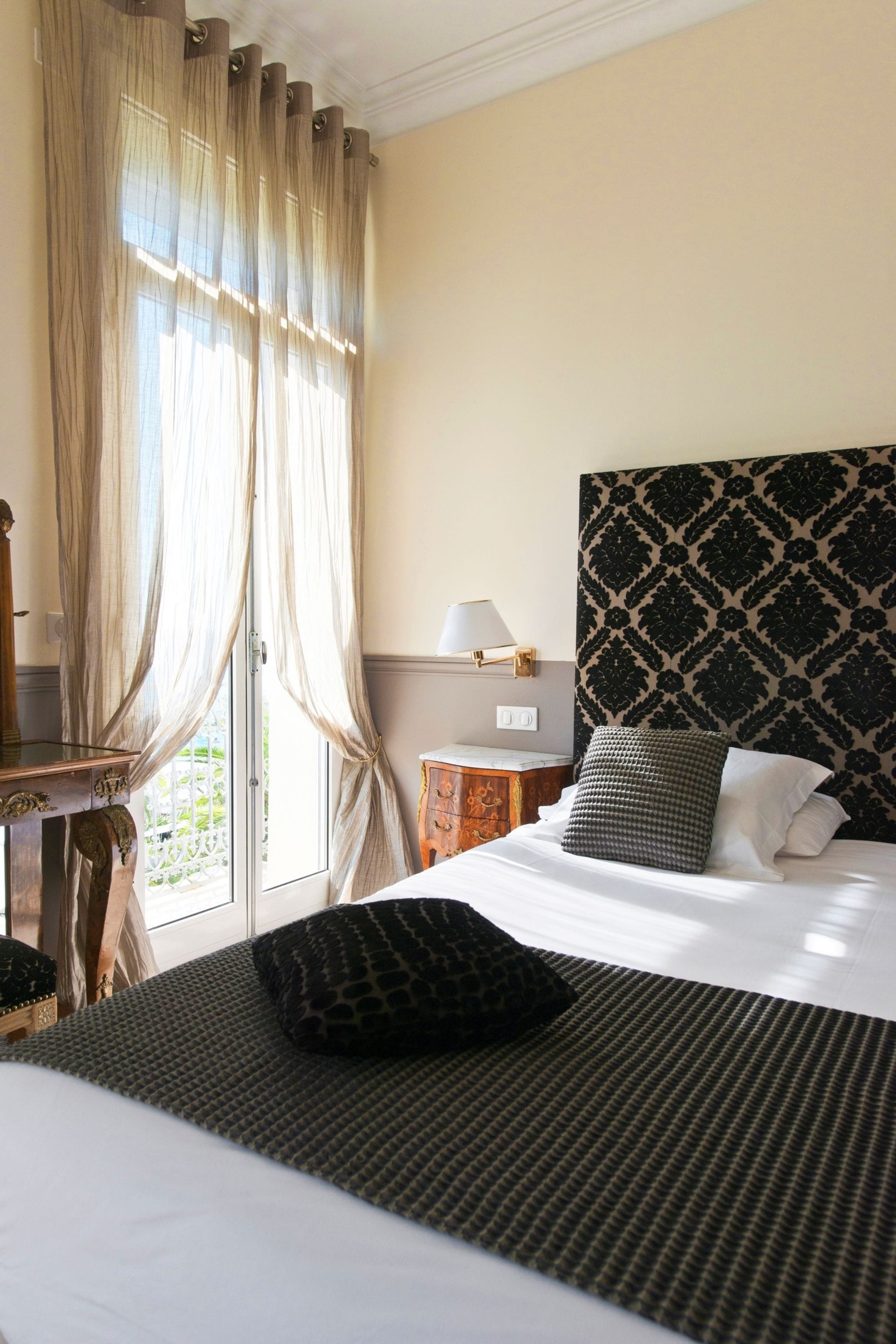 Een hotelkamer met een bed, nachtkastje, lamp en een raam met gordijnen.