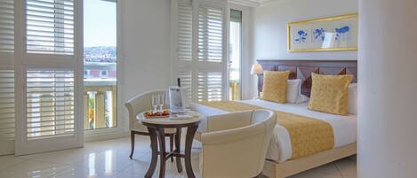 A hotel room with a bed, two chairs, a small table with glasses and a pitcher, and a window with blinds.