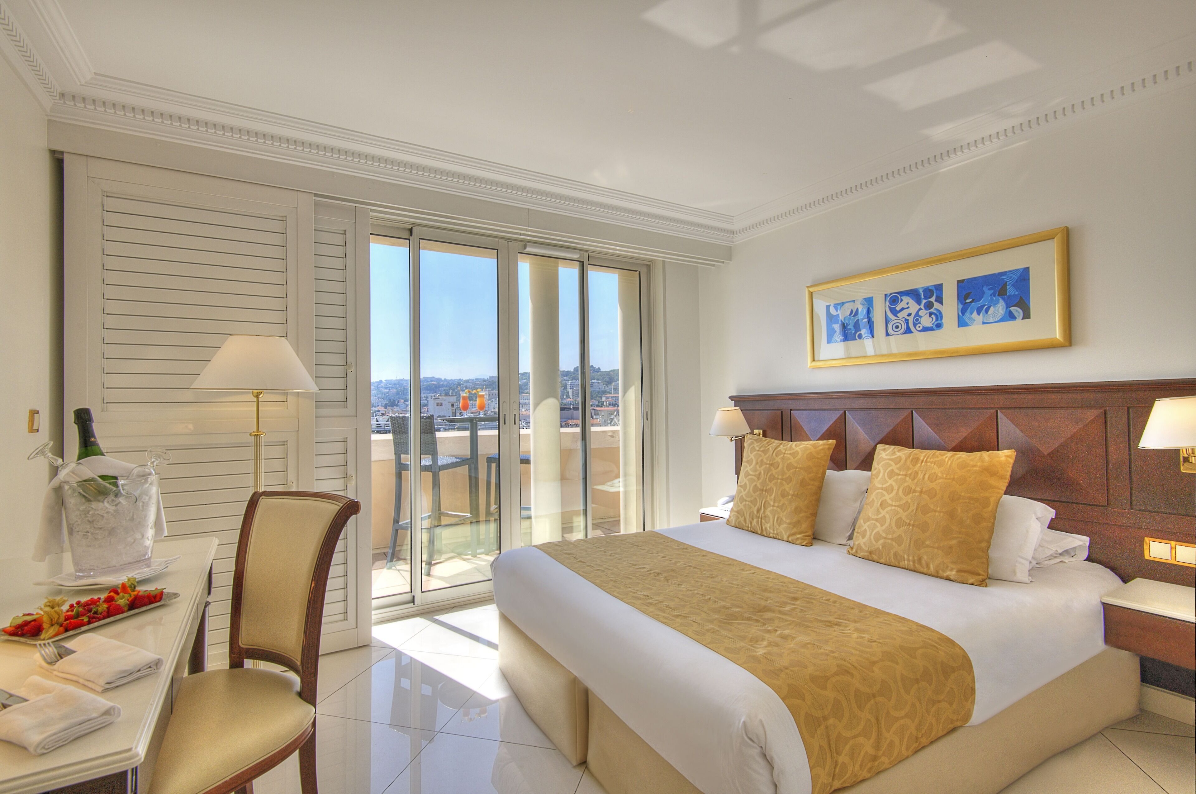 A hotel room with a large bed, a dining table with chairs, a view through the sliding doors, and a framed picture on the wall.