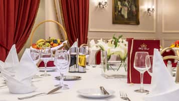 Una tavola da pranzo elegante imbandita con tovaglioli bianchi, bicchieri da vino e posate, con un cesto di frutta e i condimenti per il sale e il pepe sullo sfondo.