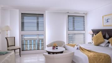 A hotel room with a bed, a chair, a small table with items on it, and a window with blinds.