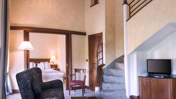Habitación de hotel con cama, una silla, una mesa con un libro, televisor y escalera.