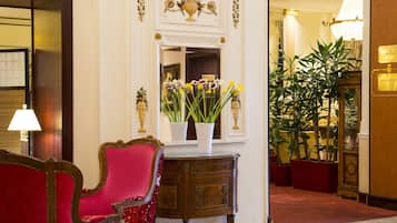 A red upholstered chair, a wooden side table with a vase of flowers, and a large mirror with a decorative frame.