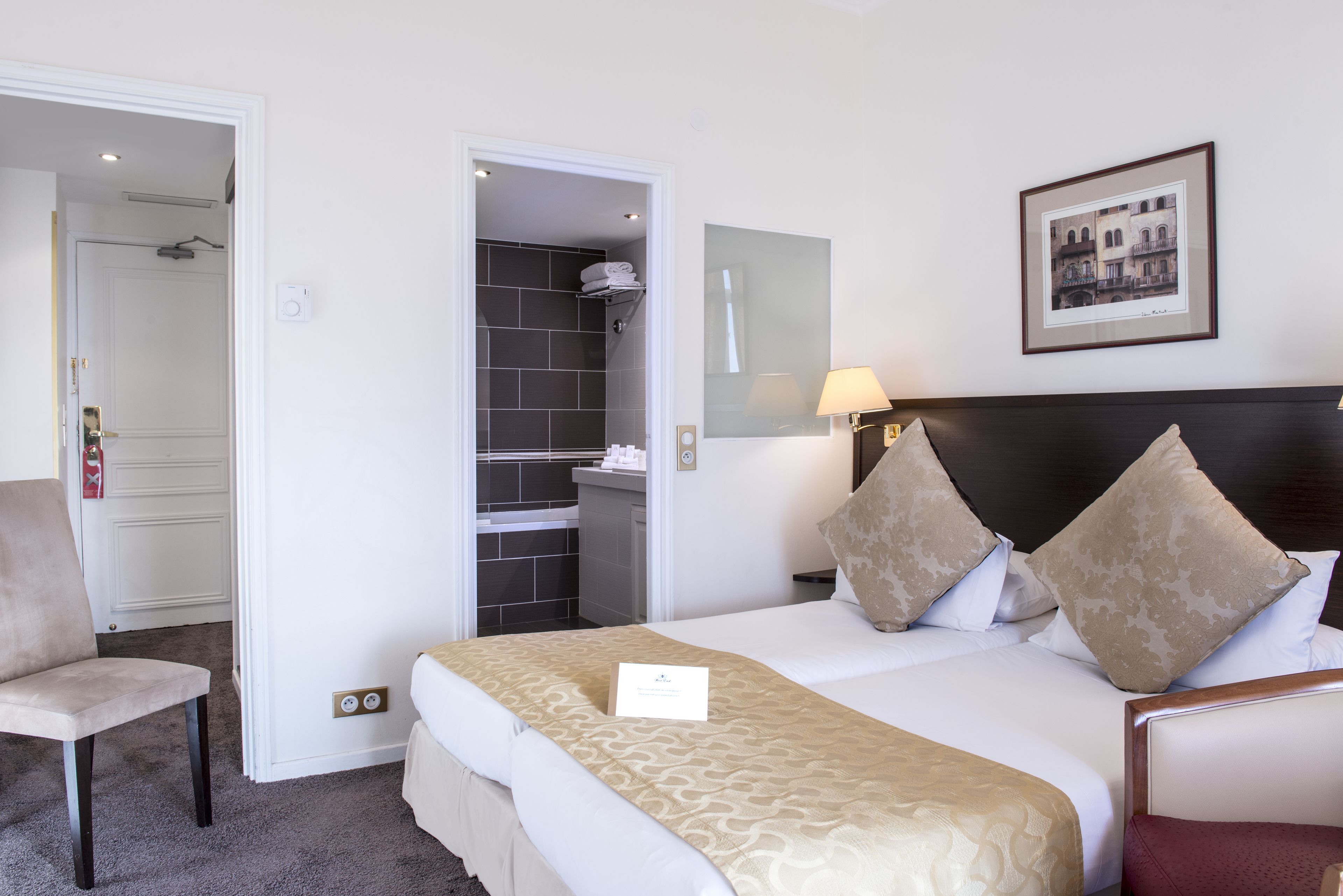 A hotel room with a bed, a chair, a wardrobe, and a bathroom visible through an open door.