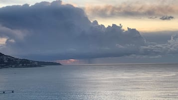 A coastal scene with a large body of water, a distant shoreline with buildings, and a dramatic sky with clouds.