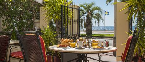A table set for breakfast with a view of the sea, surrounded by chairs with red cushions.