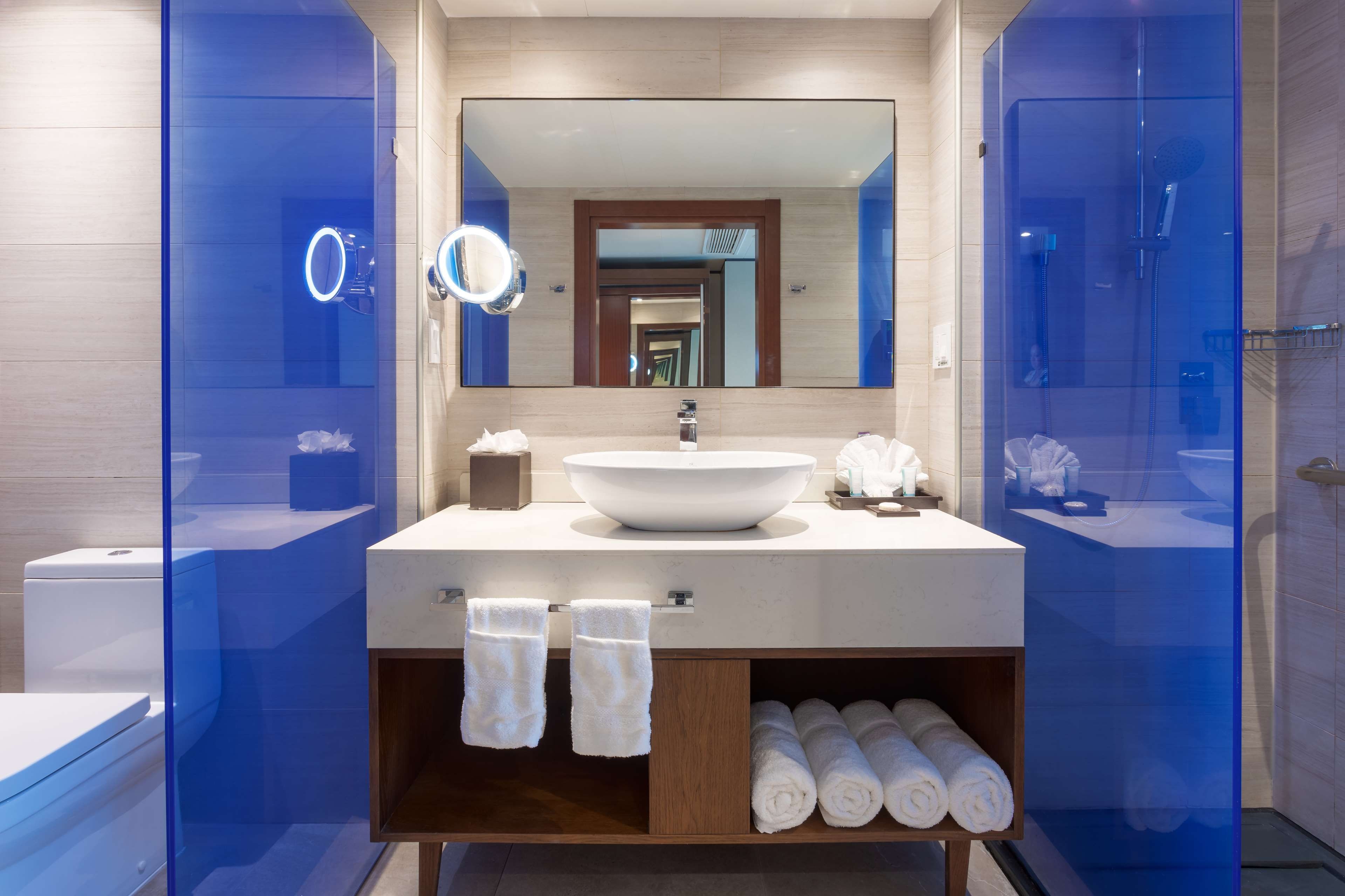 Un baño moderno con un espejo grande, un lavabo blanco y una ducha con mampara de vidrio.