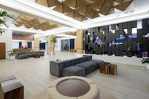 Eine großzügige Lobby mit einer breiten Eckcouch, einer runden Sitzecke und einem modernen Empfangsschalter.