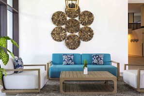 Ein modernes Wohnzimmer mit einem blauen Sofa, weißen Sesseln, einem Holztisch und einer Wanddekoration.
