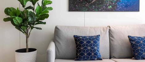 A grey sofa with two blue patterned cushions, a potted plant, and a framed picture of an underwater scene on the wall.