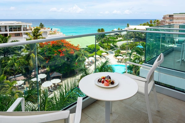 Un balcon avec une table dressée pour deux personnes, donnant sur une piscine et une plage.