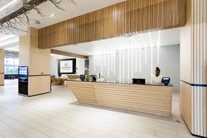 Una moderna recepción con encimera de madera, pantalla digital y zona de estar con mesas y sillas.