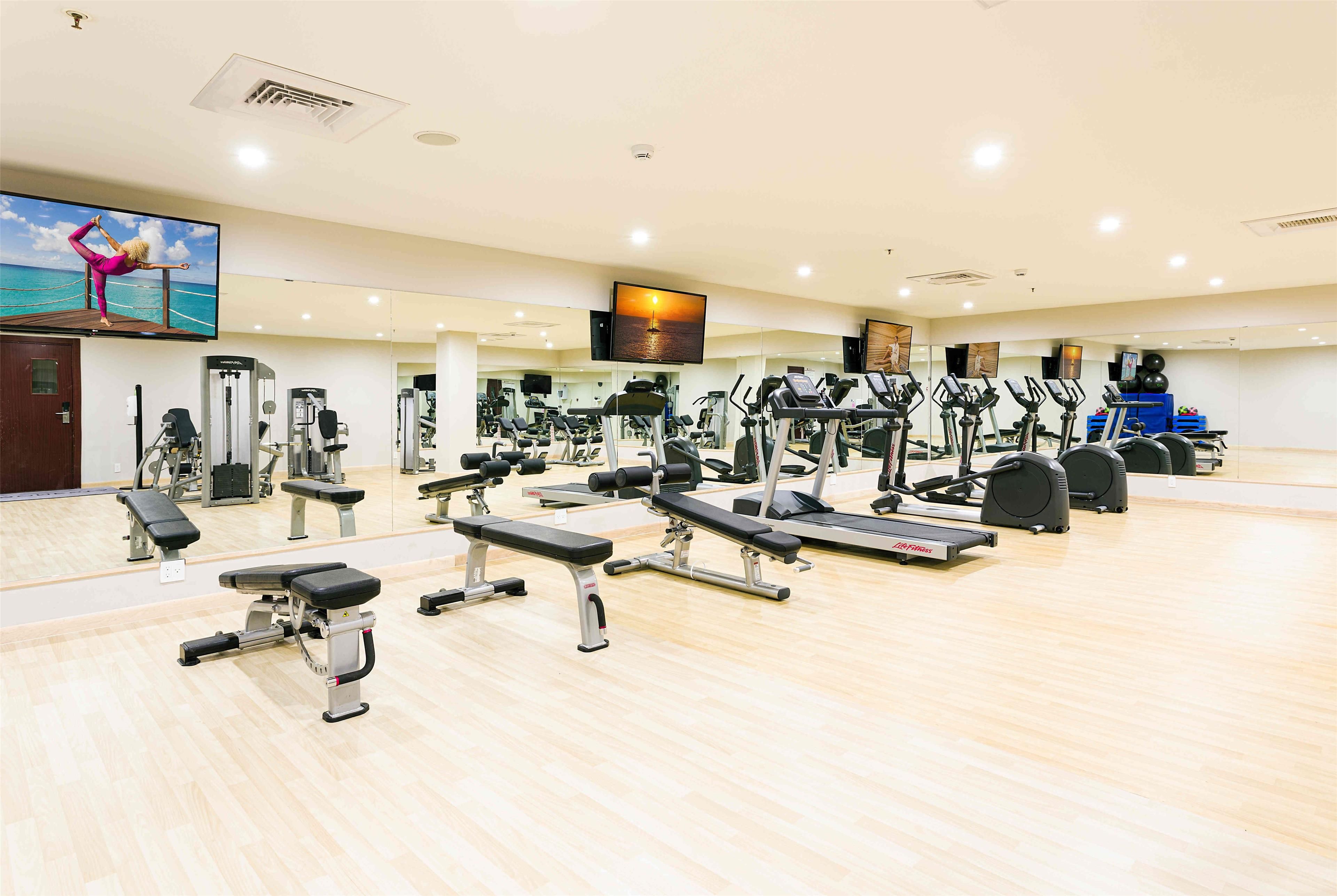 A gym with various exercise equipment, a large mirror, and a television on the wall.