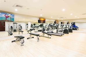 Une salle de sport équipée de divers appareils d’exercice, dotée d’un grand miroir et d’un téléviseur fixé au mur.