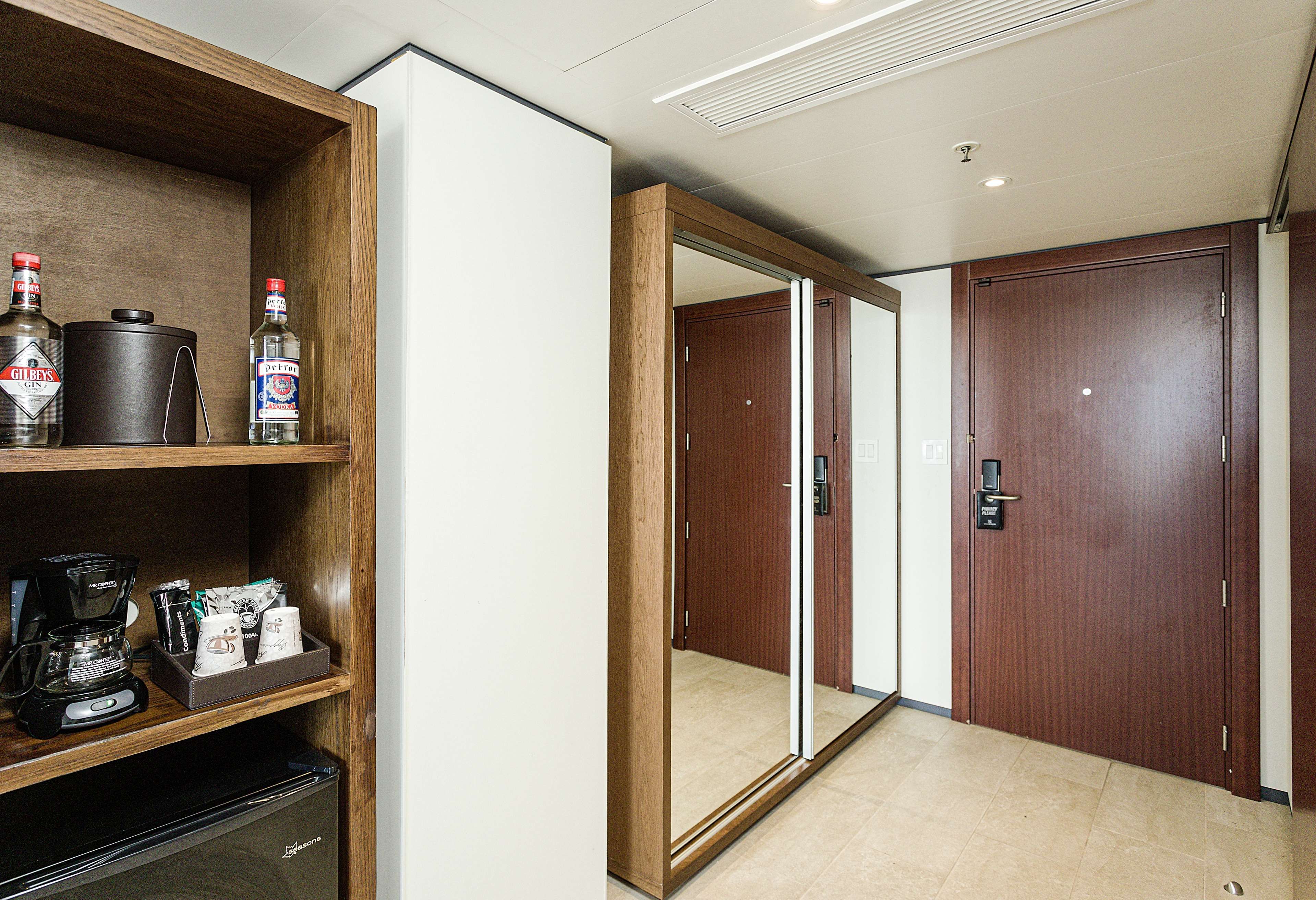 A hotel room with a minibar, a coffee machine, and a mirror.