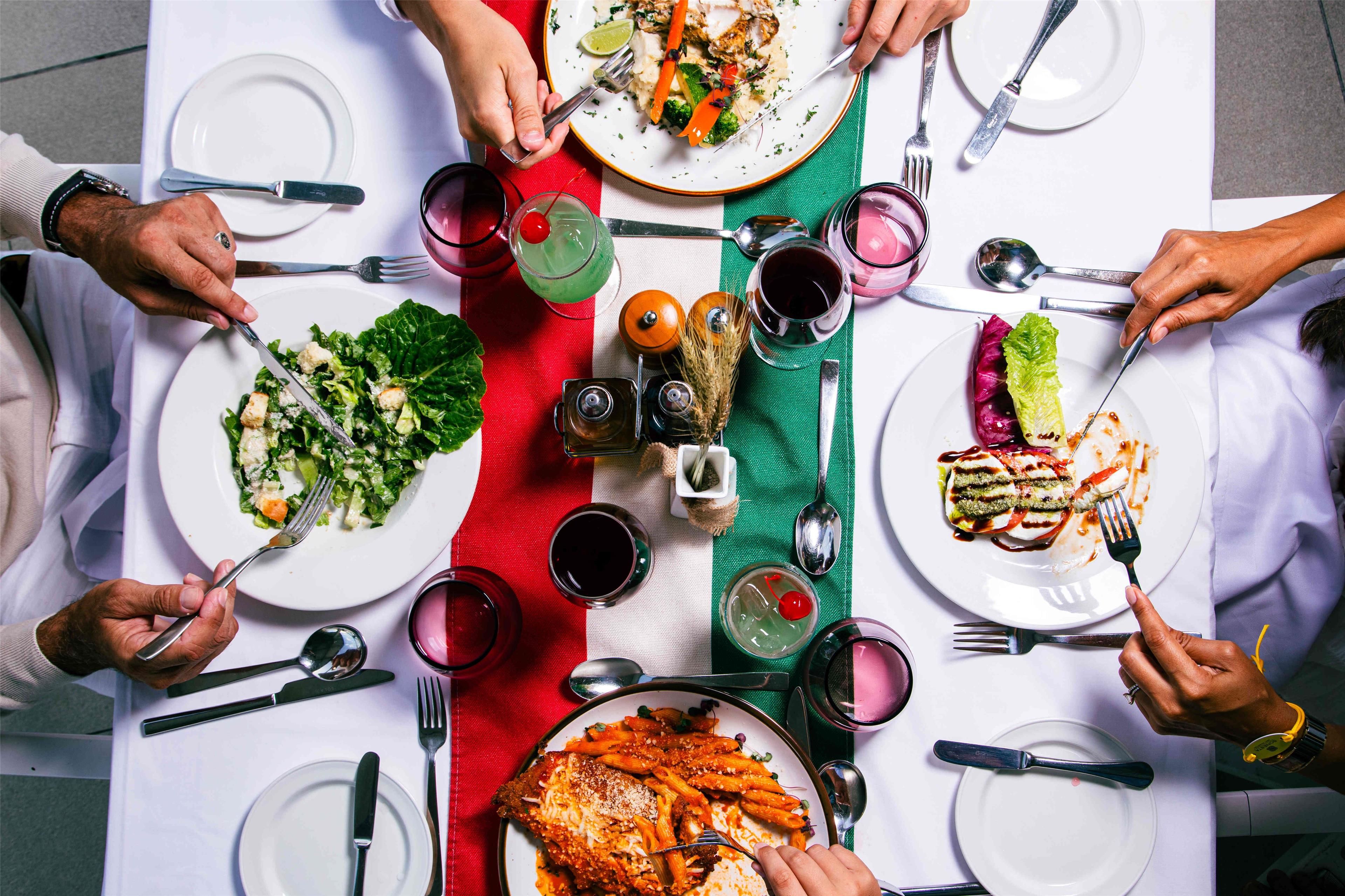A dining table with multiple plates of food, utensils, and glasses of drinks.