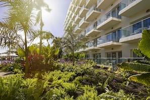 Un hôtel moderne doté d’un jardin luxuriant, de balcons avec des garde-corps en verre et offrant une vue dégagée sur le ciel.