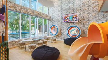 A children's play area with bean bags, circular play structures, and a large window with a view of palm trees.