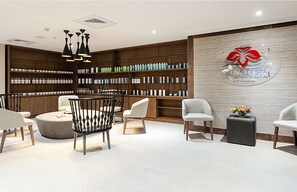 Ein Spa-Empfangsbereich mit einem Holzbüro, weißen Stühlen und einer Wand mit einem Logo sowie Produktregalen.