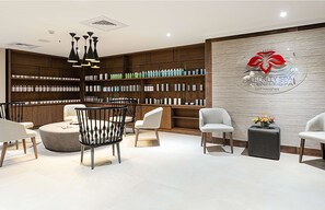 A spa reception area with a wooden reception desk, white chairs, and a wall with a logo and shelves of products.