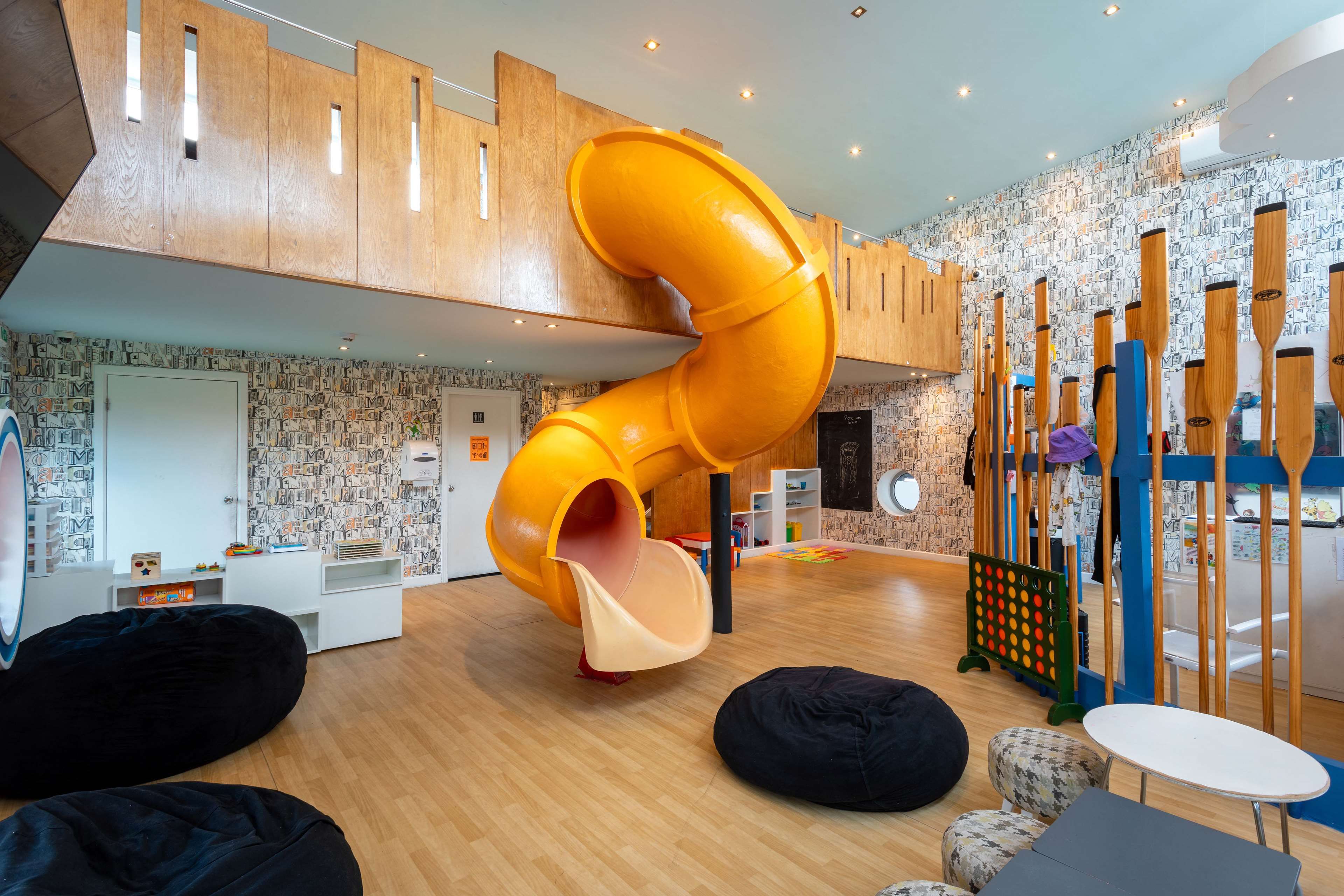 Un espace de jeux pour enfants avec un toboggan, des poufs et un parc.