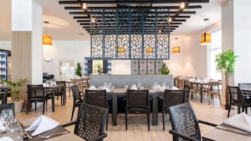 Un restaurante con una decoración moderna, con sillas de mimbre negro, mesas de madera y un techo decorativo con luces colgantes.
