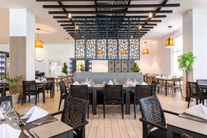 A restaurant with a modern interior, featuring black wicker chairs, wooden tables, and a decorative ceiling with hanging lights. - Sonesta Maho Beach All Inclusive Resort Casino & Spa (Lowlands)