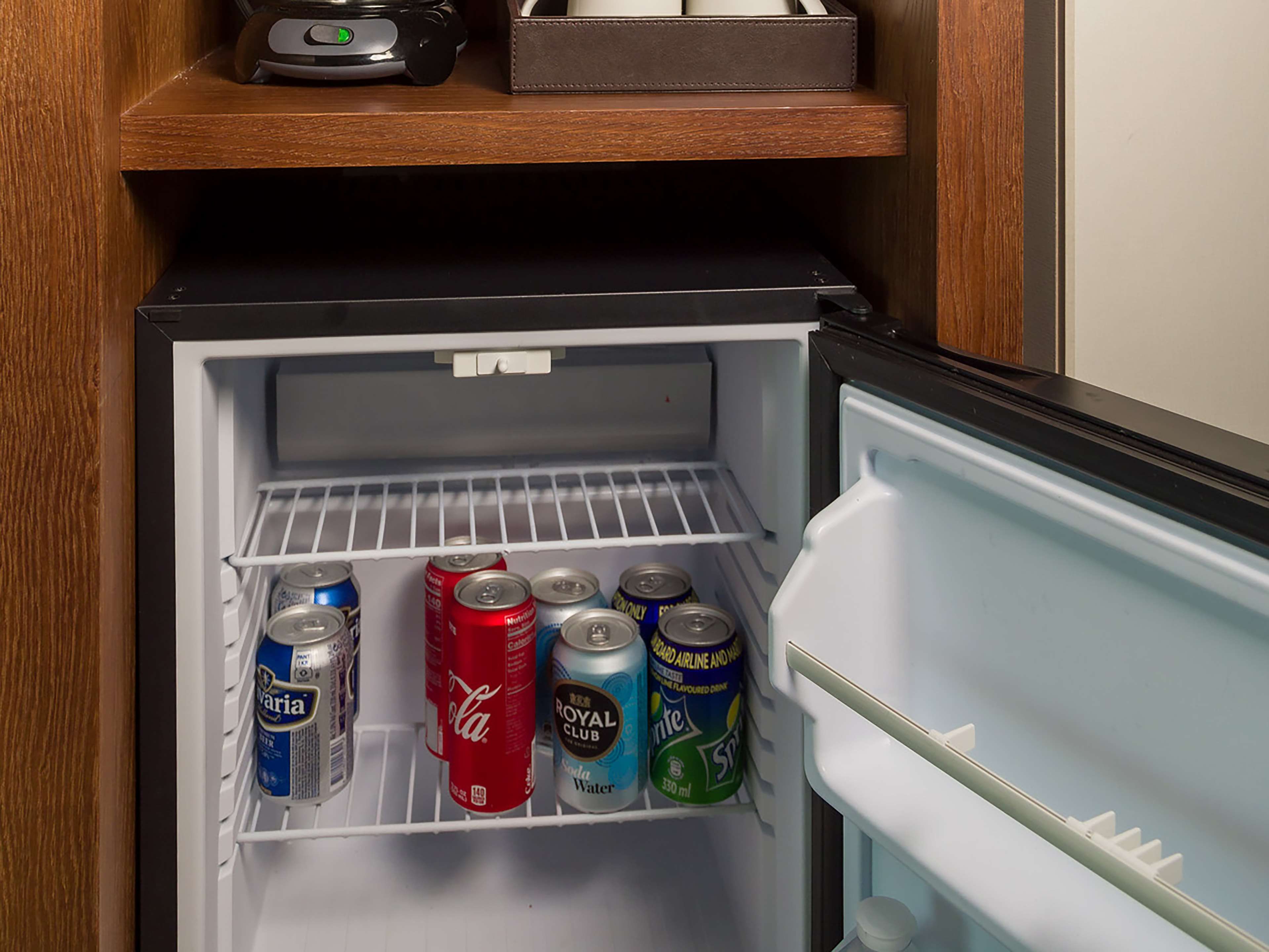 Un réfrigérateur avec des étagères contenant diverses boissons, notamment des canettes de soda et une bouteille d’eau.