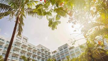 Un hotel de varios pisos con balcones y un patio rodeado de palmeras y plantas tropicales.