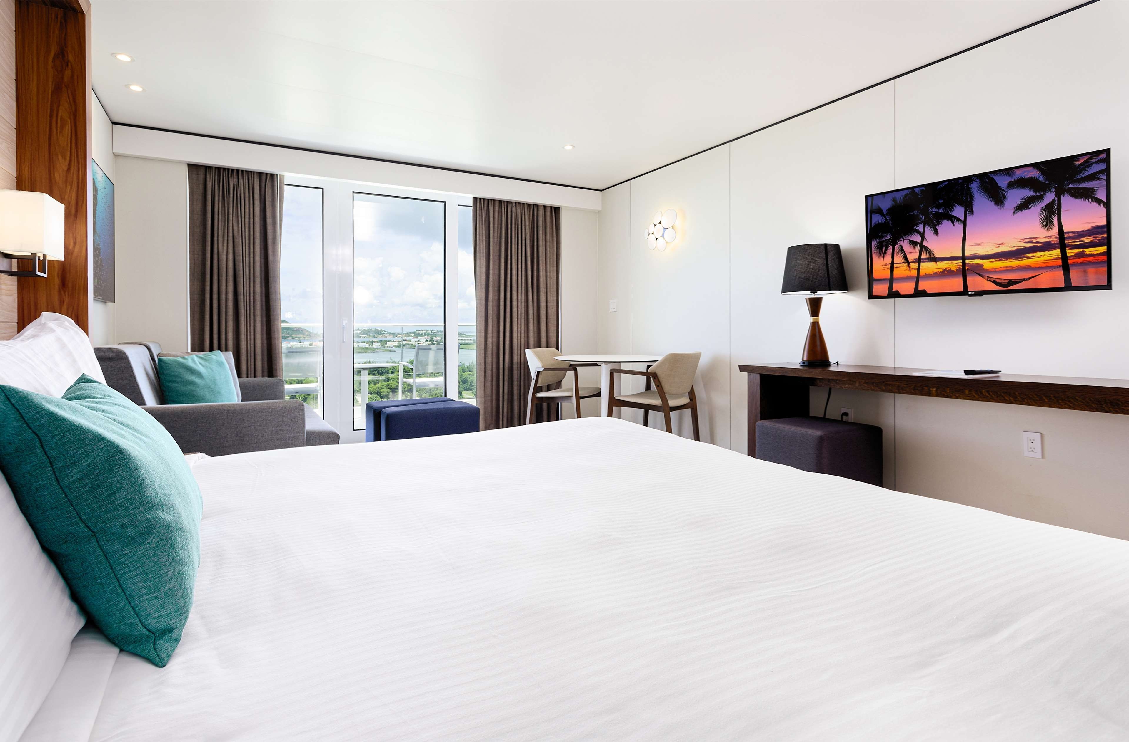 Une chambre d’hôtel moderne dotée d’un grand lit, d’un bureau, d’une chaise et offrant une vue sur la ville grâce à de grandes fenêtres.