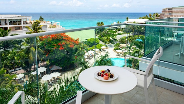 Un balcón con mesa para dos, con vistas a una piscina y una playa.