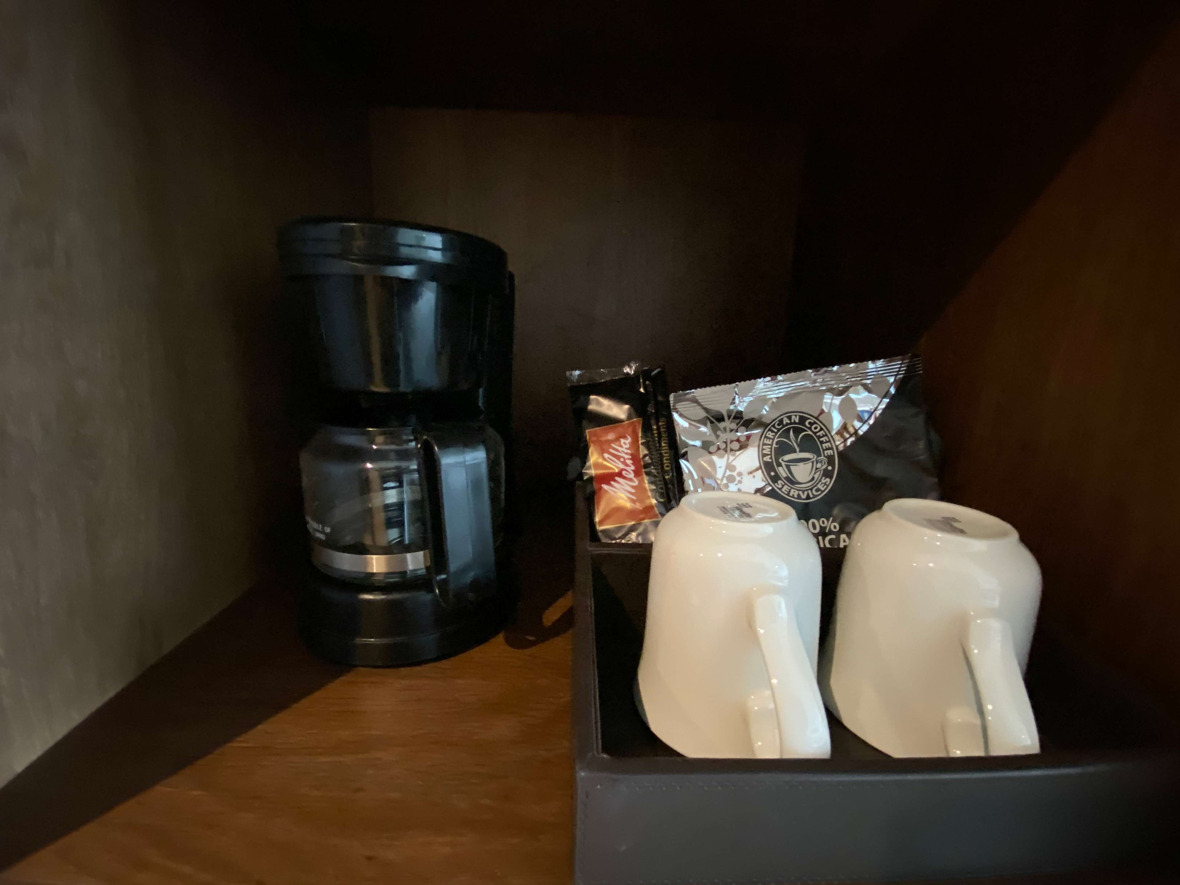 A coffee maker, two white mugs, and a coffee pod on a shelf.