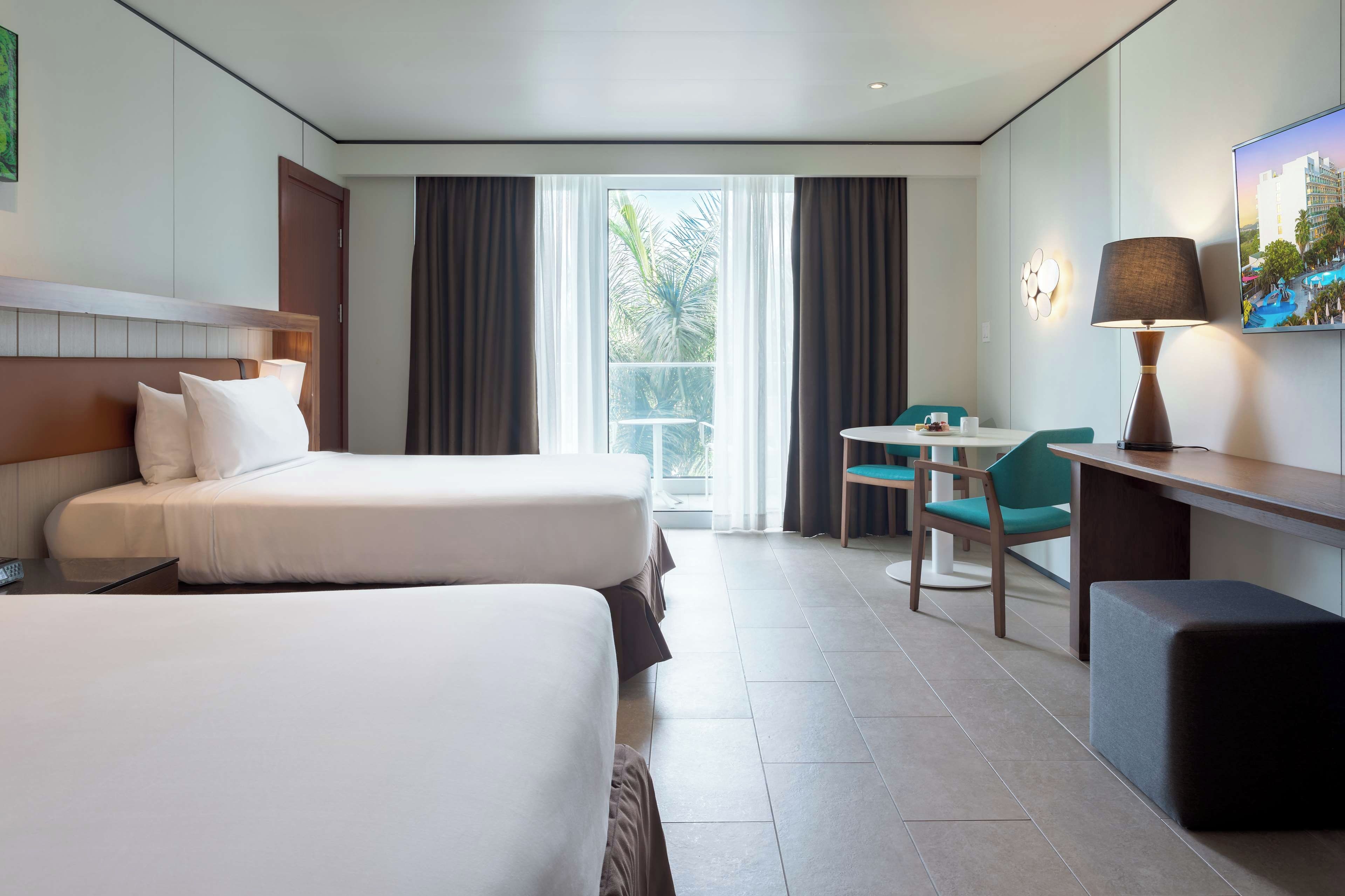 A hotel room with two beds, a desk, a chair, and a TV.