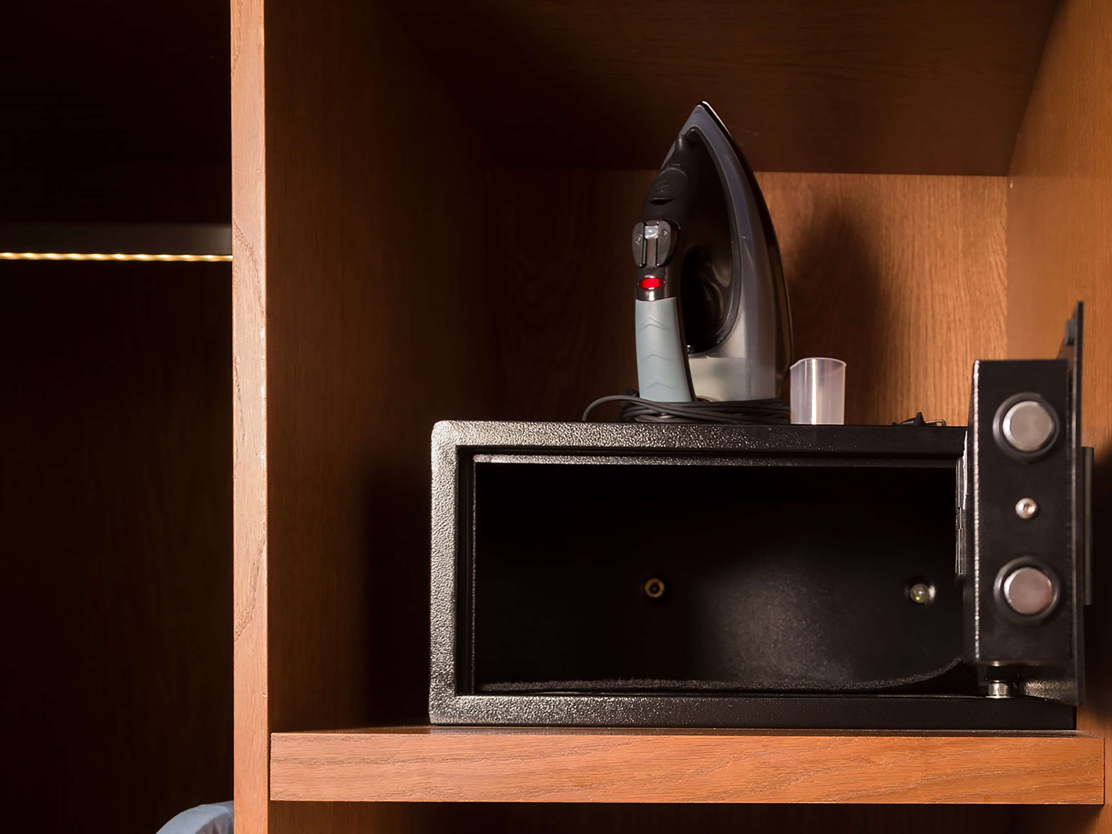 A compact microwave with a control panel and a small cup holder in a wooden cabinet.