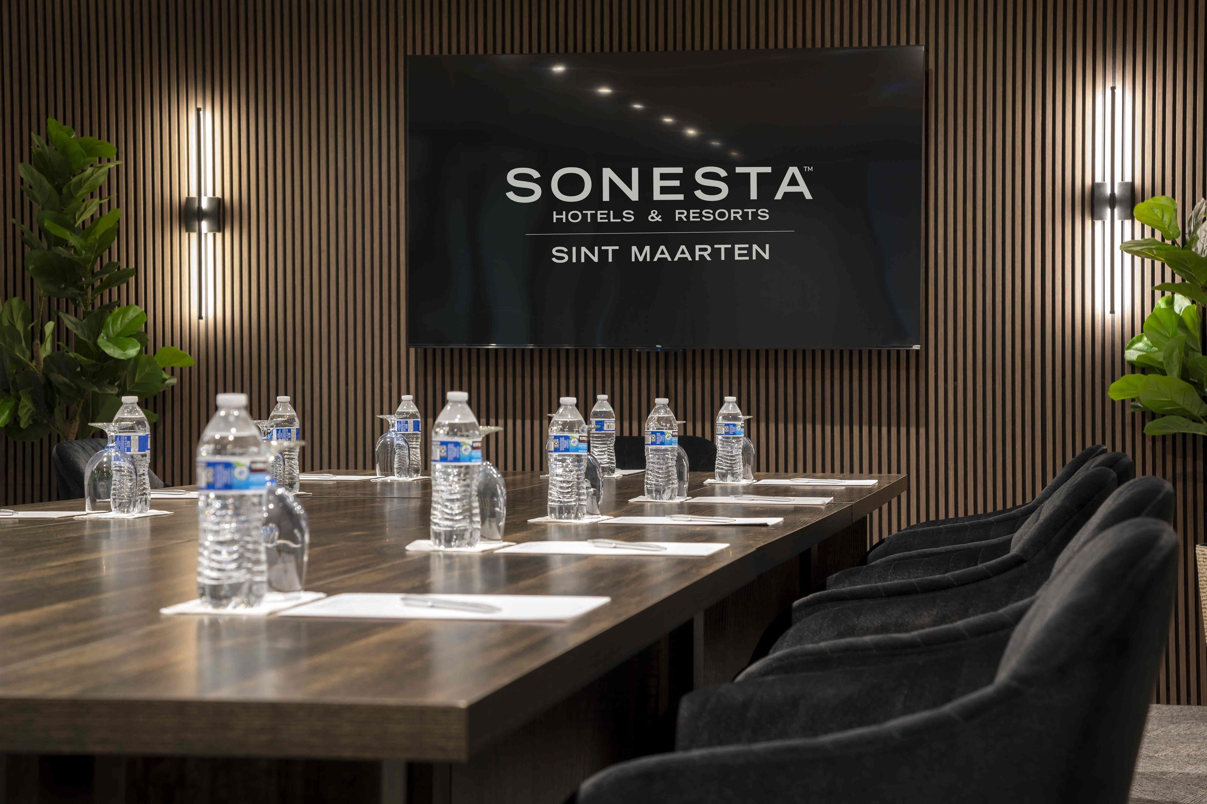 A conference room with a long table, water bottles, and a TV displaying 'SONESTA HOTELS & RESORTS SINT MAARTEN'.