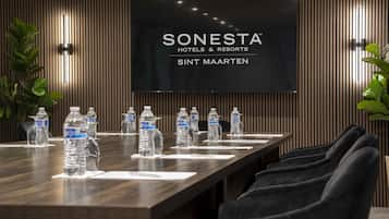 Une salle de conférence avec une longue table, des bouteilles d’eau et un téléviseur affichant le texte « SONESTA HOTELS & RESORTS SINT MAARTEN ».