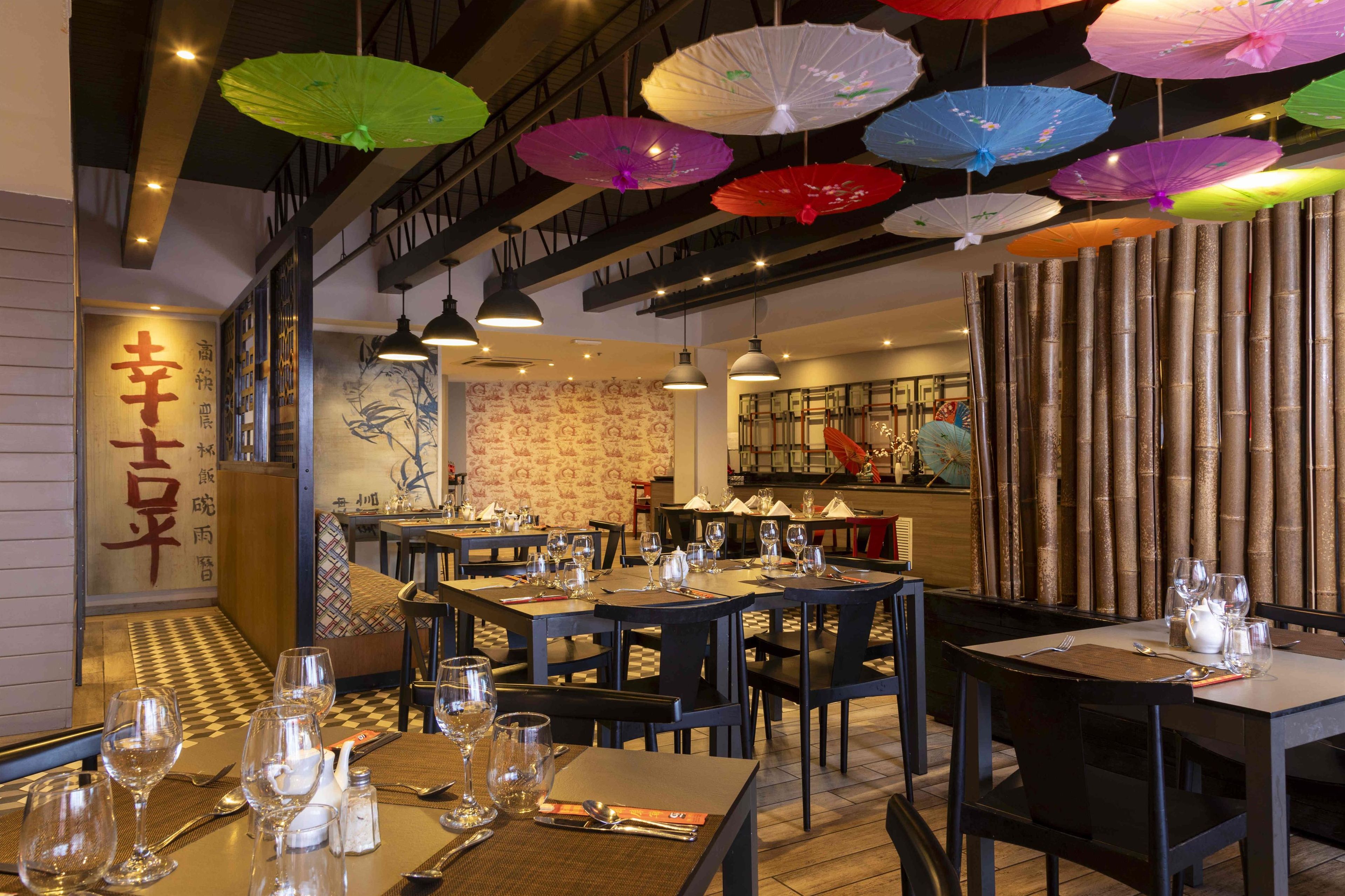 A restaurant interior with tables set for dining, hanging umbrellas, and traditional decor.