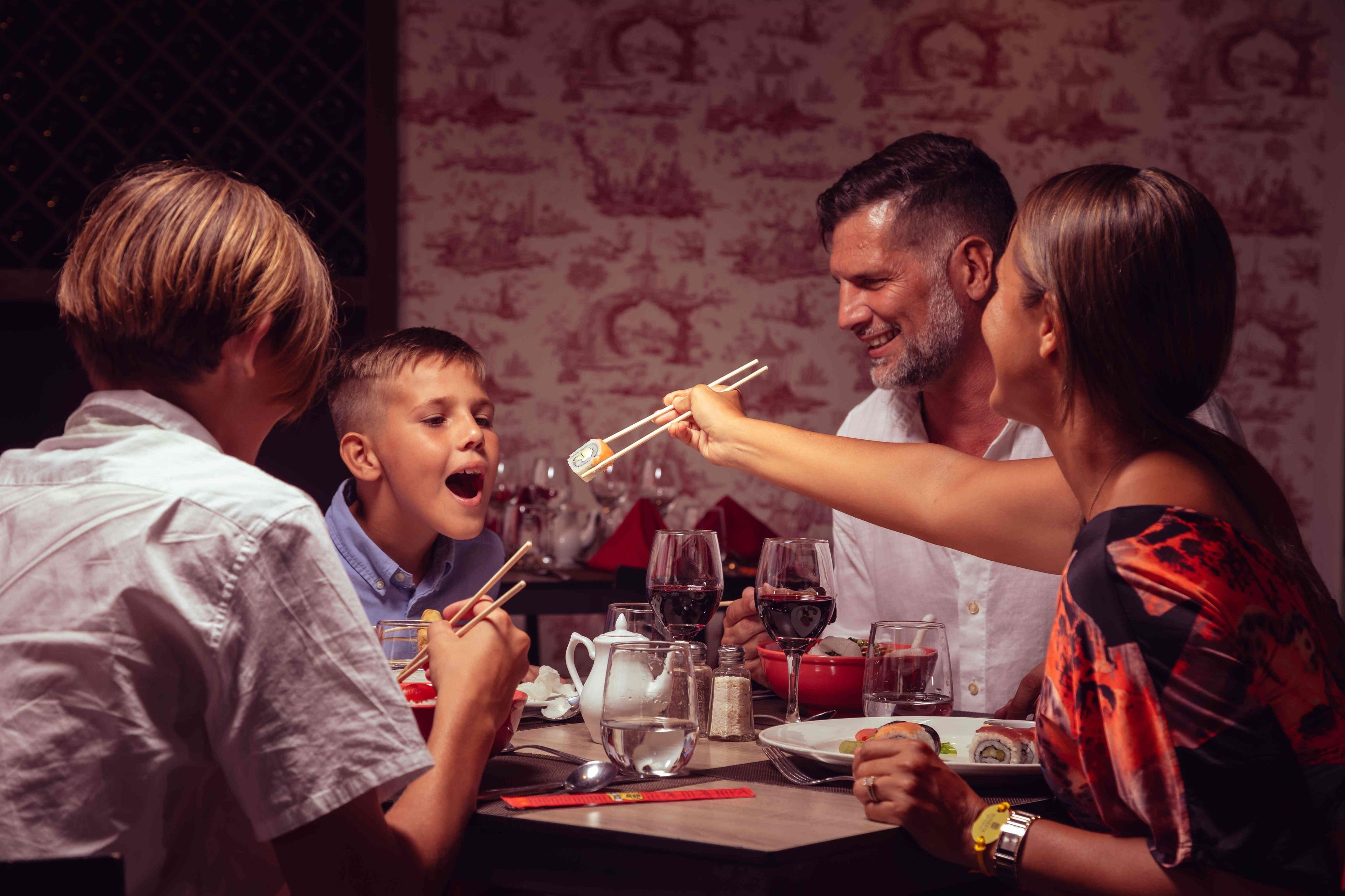 Una familia cenando en una mesa con copas de vino, palillos y una tetera.