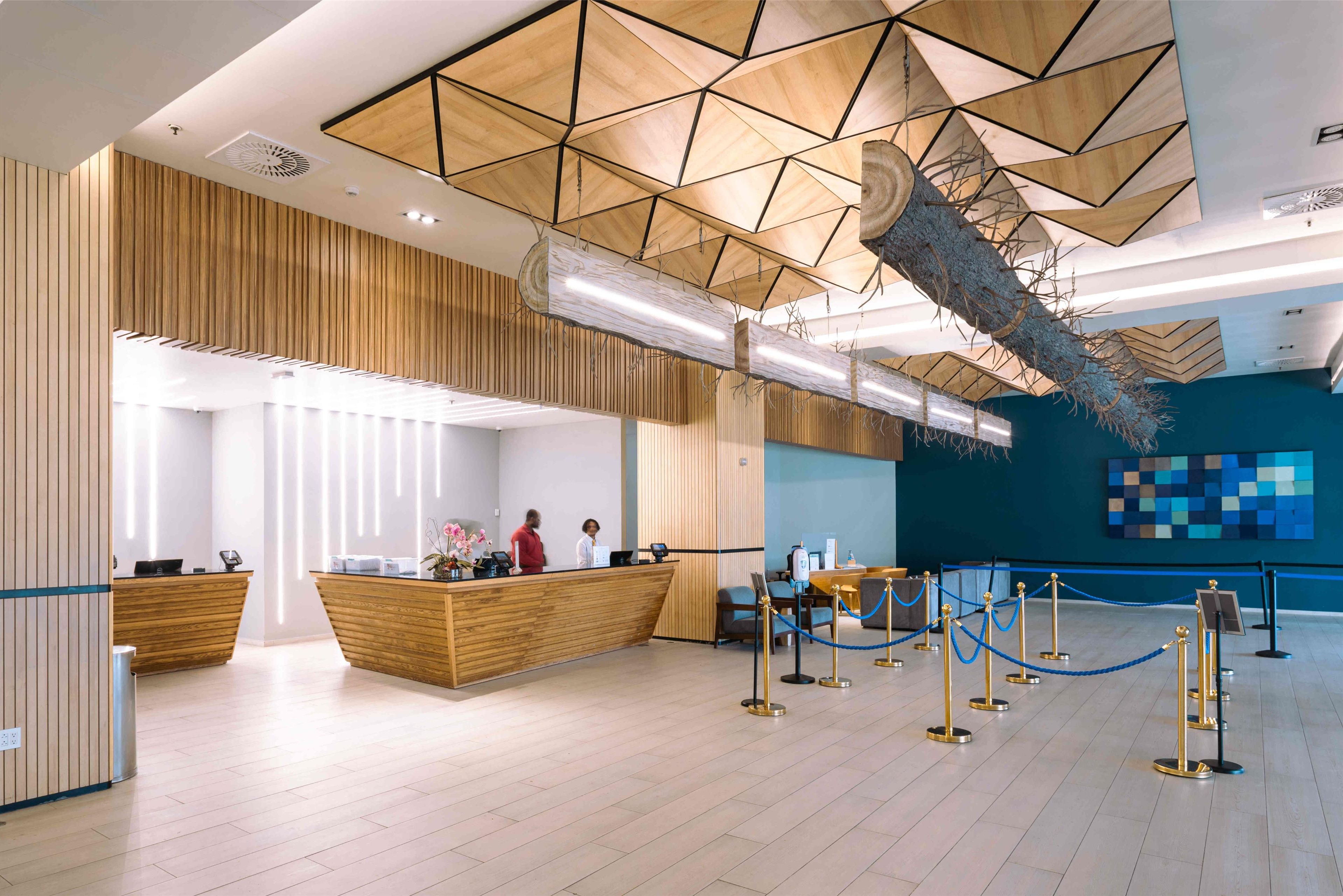A modern reception area with wooden reception desks, a blue seating area, and a geometric ceiling design.